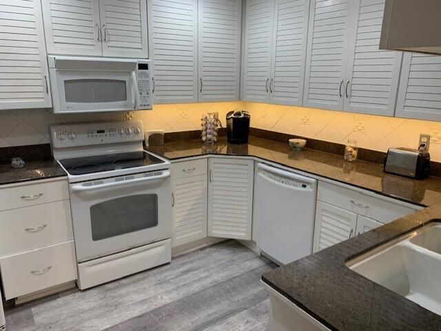 kitchen featuring white appliances, light hardwood / wood-style flooring, white cabinetry, and backsplash