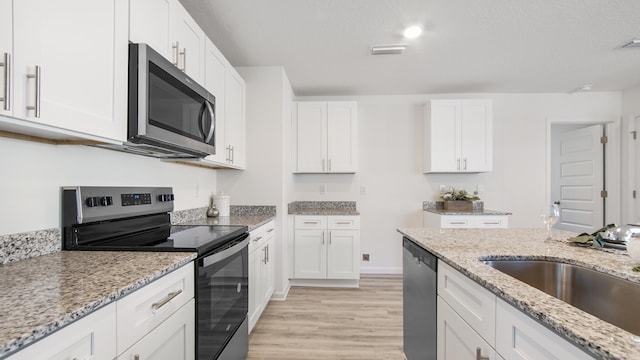 kitchen with light stone countertops, stainless steel appliances, white cabinets, and sink