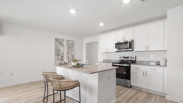 kitchen featuring light stone countertops, white cabinetry, appliances with stainless steel finishes, and a kitchen island with sink