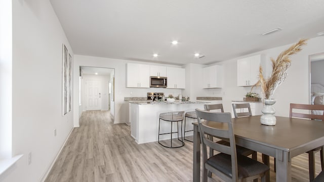 kitchen featuring white cabinetry, light hardwood / wood-style floors, a breakfast bar area, a kitchen island, and light stone counters