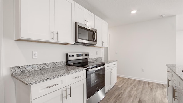 kitchen featuring light wood-type flooring, stainless steel appliances, white cabinets, and light stone counters