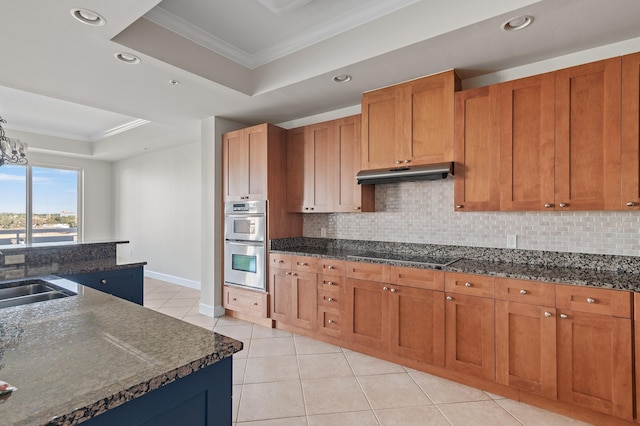 kitchen with an inviting chandelier, a raised ceiling, decorative backsplash, ornamental molding, and double oven