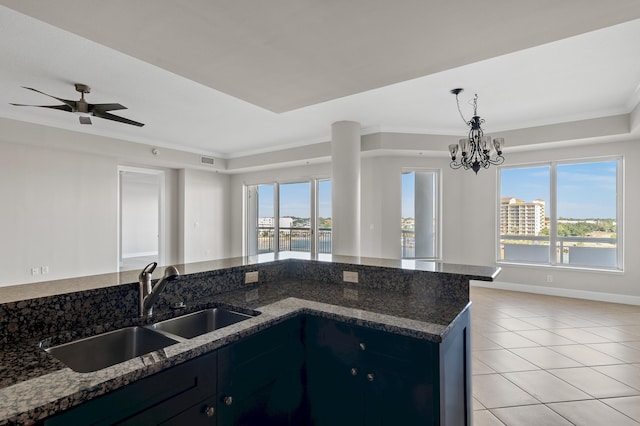 kitchen featuring plenty of natural light, dark stone counters, ceiling fan with notable chandelier, and sink