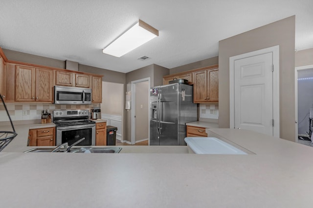 kitchen with a textured ceiling, sink, backsplash, and appliances with stainless steel finishes