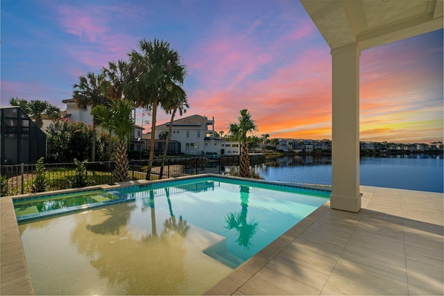 pool at dusk featuring a water view and a patio area