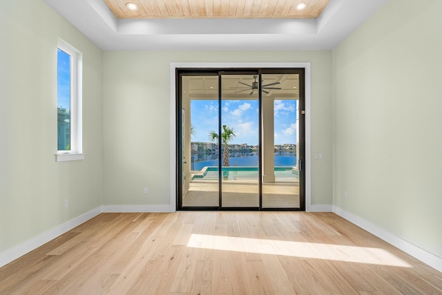 spare room featuring a water view, ceiling fan, a tray ceiling, and light hardwood / wood-style floors