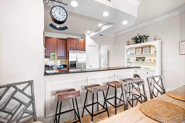 kitchen featuring tasteful backsplash, stainless steel fridge with ice dispenser, kitchen peninsula, crown molding, and a breakfast bar area