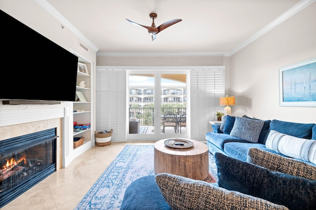 tiled living room with built in shelves, ceiling fan, a fireplace, and ornamental molding