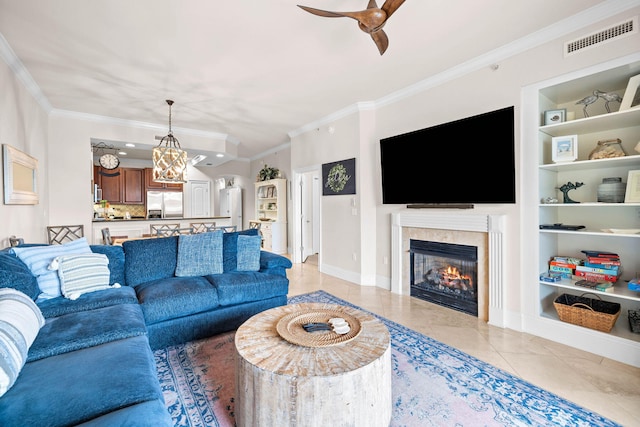 tiled living room featuring built in shelves, ceiling fan with notable chandelier, and ornamental molding