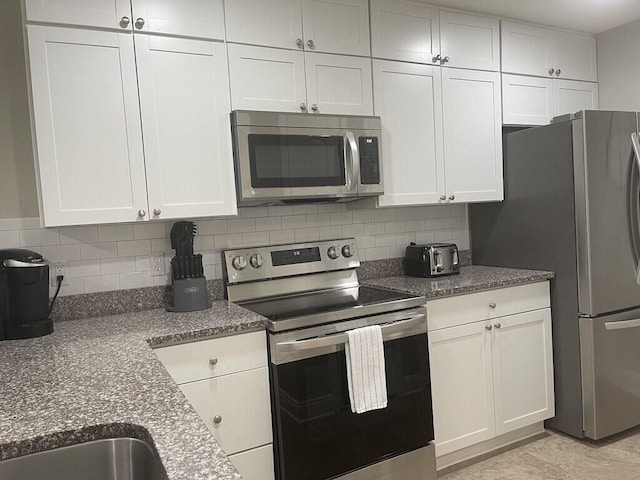 kitchen featuring white cabinets, decorative backsplash, stainless steel appliances, and dark stone counters