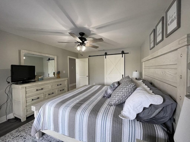 bedroom with a barn door, ceiling fan, and dark hardwood / wood-style floors