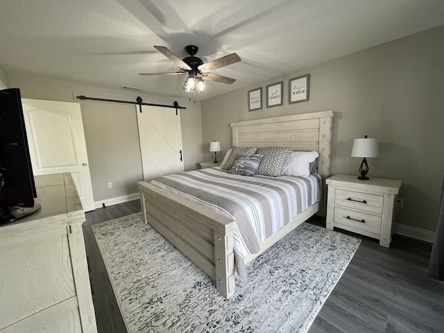 bedroom with a barn door, ceiling fan, and dark hardwood / wood-style flooring