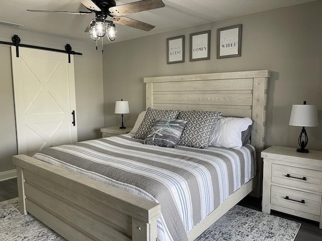 bedroom with wood-type flooring, a barn door, and ceiling fan