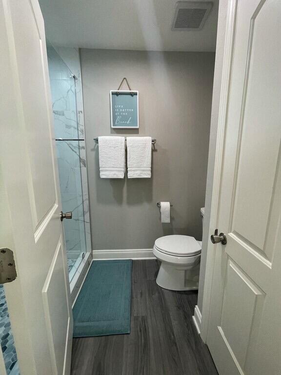 bathroom with tiled shower, toilet, and hardwood / wood-style flooring