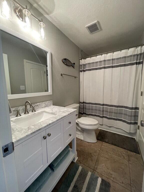 bathroom featuring a shower with curtain, tile patterned floors, a textured ceiling, toilet, and vanity