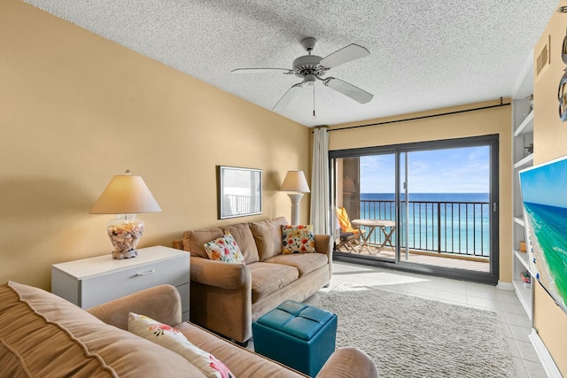 tiled living room featuring ceiling fan, a water view, and a textured ceiling