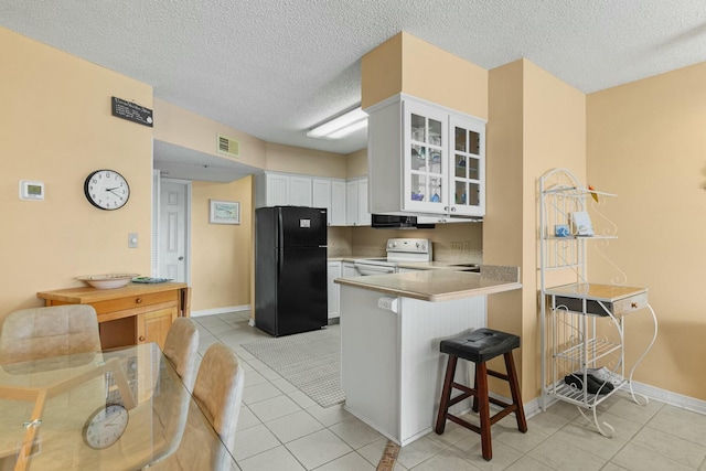 kitchen featuring white electric range, kitchen peninsula, a kitchen bar, black refrigerator, and white cabinets