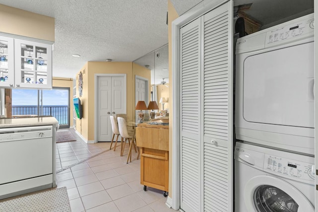 washroom with a textured ceiling, stacked washer and clothes dryer, and light tile patterned flooring