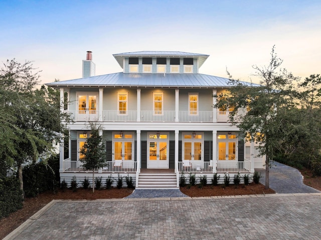 back house at dusk with french doors, a balcony, and covered porch