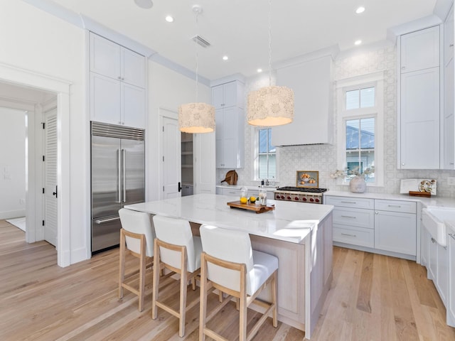 kitchen featuring pendant lighting, a center island, wall chimney exhaust hood, stainless steel built in fridge, and backsplash