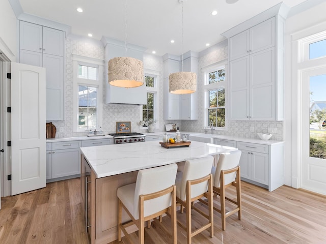 kitchen with range, a center island, white cabinetry, hanging light fixtures, and light hardwood / wood-style flooring