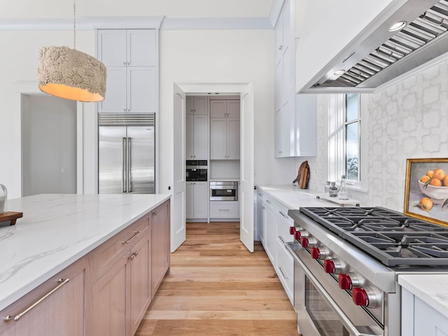 kitchen featuring light stone countertops, premium appliances, wall chimney range hood, and white cabinetry