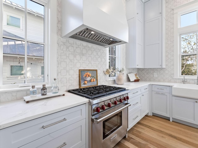 kitchen with a wealth of natural light, decorative backsplash, wall chimney range hood, and designer range