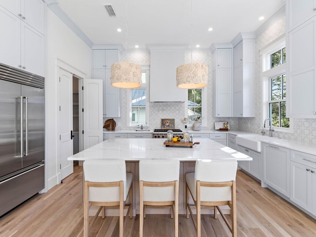 kitchen featuring decorative light fixtures, a center island, sink, light stone countertops, and stainless steel built in fridge