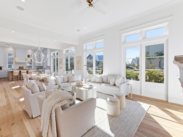 living room featuring plenty of natural light, ceiling fan with notable chandelier, ornamental molding, and light hardwood / wood-style flooring