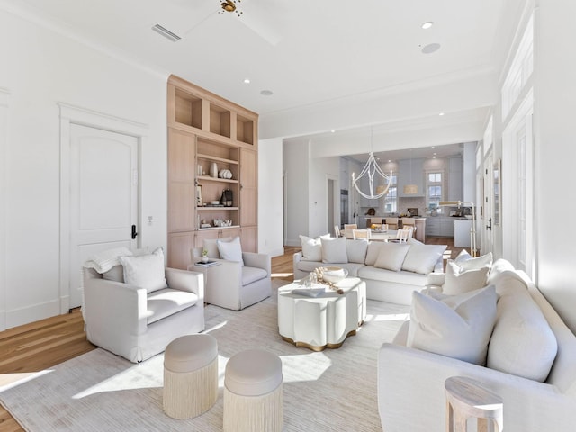 living room featuring built in shelves, light wood-type flooring, ornamental molding, and an inviting chandelier