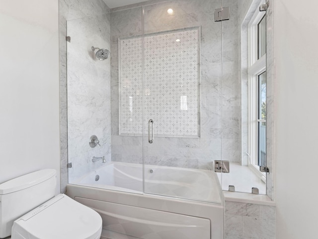 bathroom featuring toilet and shower / bath combination with glass door