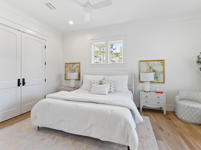 bedroom with ceiling fan, light wood-type flooring, crown molding, and a closet