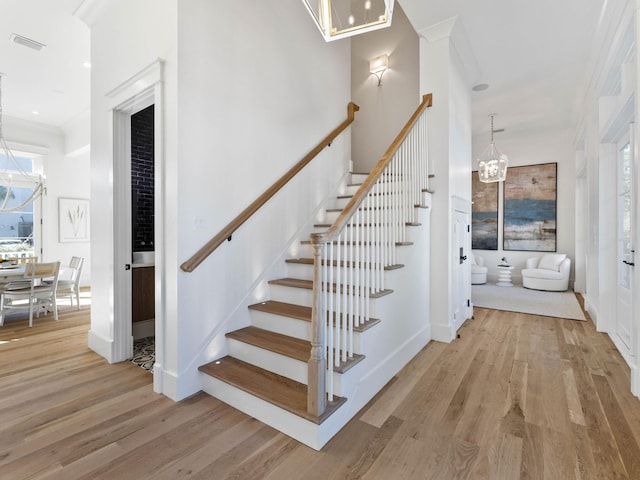 stairs with an inviting chandelier, ornamental molding, and wood-type flooring