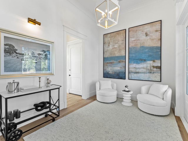 sitting room with crown molding, a notable chandelier, and light wood-type flooring