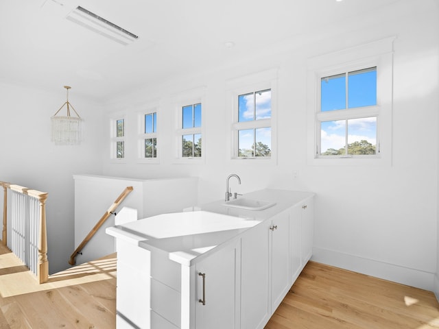 kitchen with decorative light fixtures, white cabinetry, light hardwood / wood-style floors, sink, and kitchen peninsula