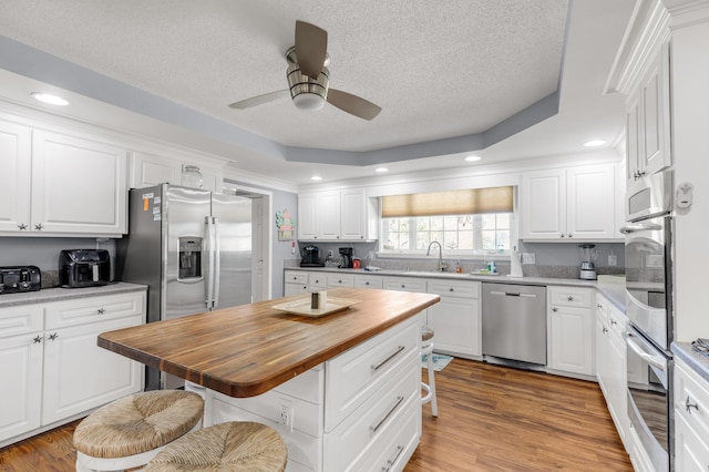 kitchen featuring white cabinetry, a center island, stainless steel appliances, wood counters, and a kitchen breakfast bar