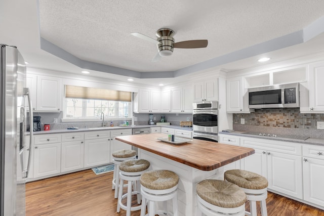 kitchen with a kitchen breakfast bar, light wood-type flooring, stainless steel appliances, white cabinetry, and butcher block counters