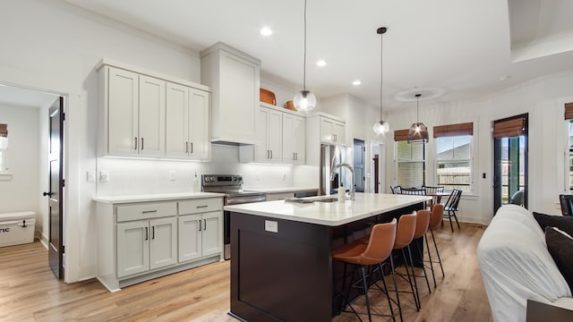 kitchen with a kitchen bar, appliances with stainless steel finishes, light wood-type flooring, hanging light fixtures, and an island with sink