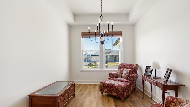 living area featuring a chandelier, a raised ceiling, and light hardwood / wood-style flooring