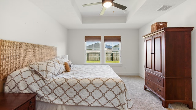 carpeted bedroom with a raised ceiling and ceiling fan