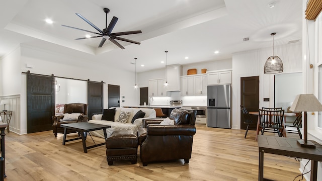 living room featuring light wood-type flooring, a barn door, a tray ceiling, and ceiling fan