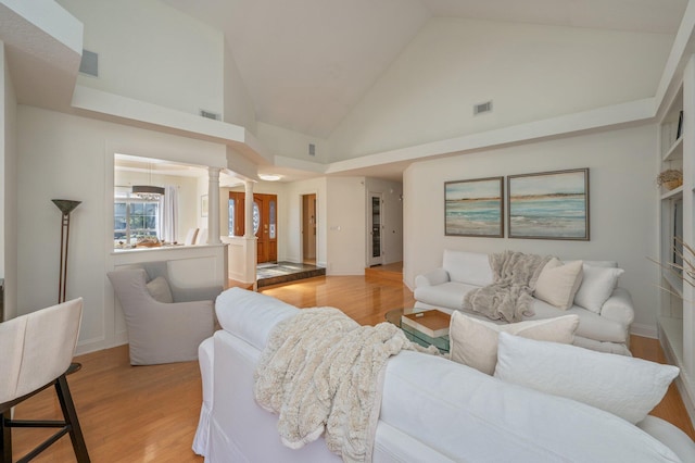 living room featuring light wood-type flooring, high vaulted ceiling, and decorative columns