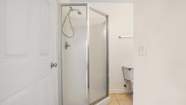 bathroom featuring tile patterned flooring, a shower with shower door, and toilet