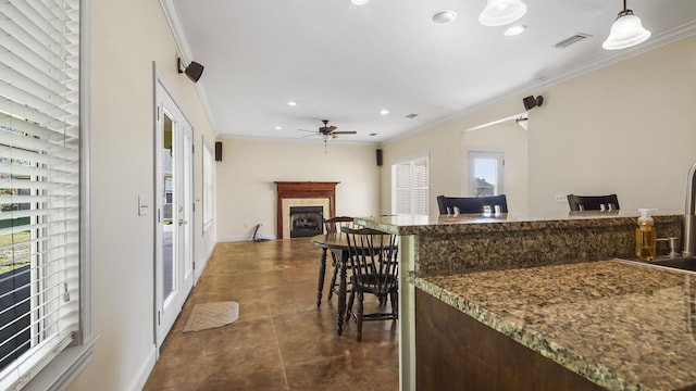 kitchen with ceiling fan, a breakfast bar, dark stone counters, and ornamental molding