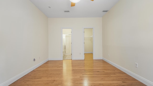 unfurnished bedroom with ceiling fan, a spacious closet, light wood-type flooring, connected bathroom, and a closet