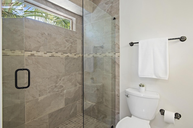 bathroom featuring a shower with door and toilet