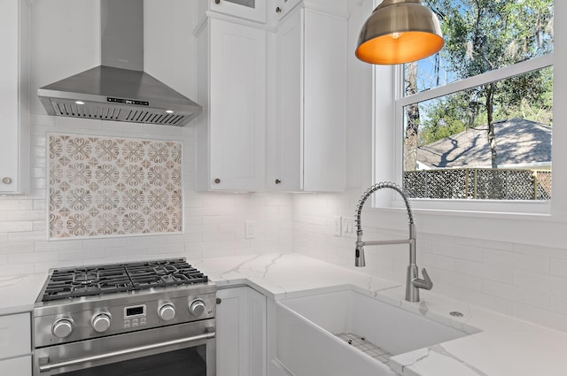 kitchen with sink, high end stainless steel range, wall chimney exhaust hood, light stone countertops, and white cabinetry