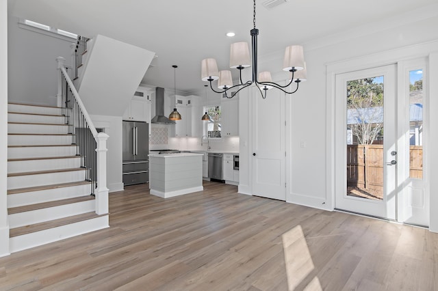 kitchen featuring appliances with stainless steel finishes, wall chimney range hood, decorative light fixtures, white cabinets, and a kitchen island