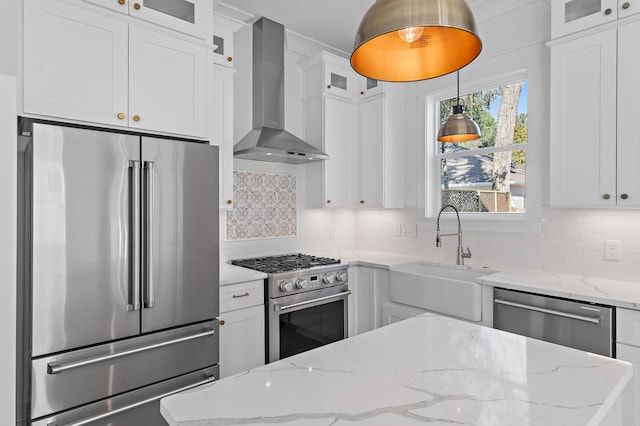 kitchen with hanging light fixtures, white cabinetry, high end appliances, and wall chimney exhaust hood