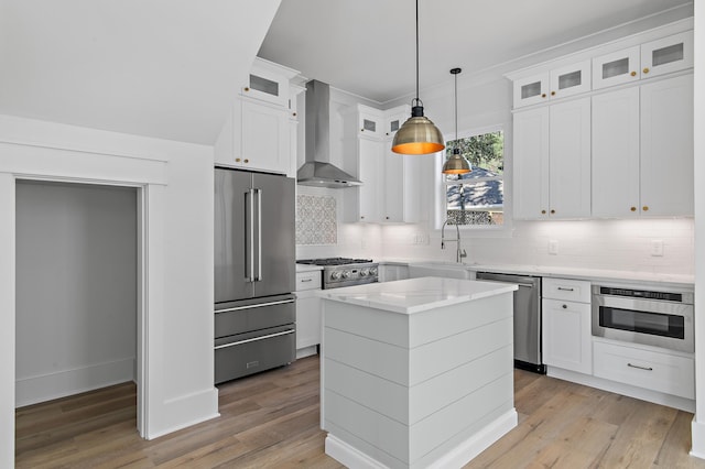 kitchen featuring wall chimney exhaust hood, a kitchen island, white cabinetry, and appliances with stainless steel finishes